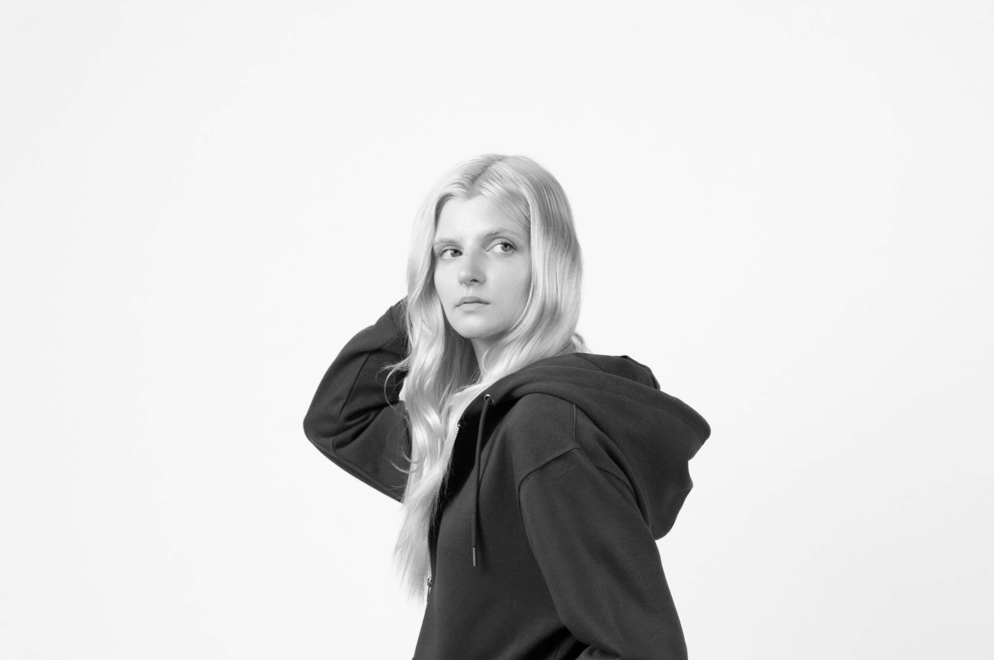 Closeup of a woman viewed from the side wearing a hoodie. Image is in black and white.